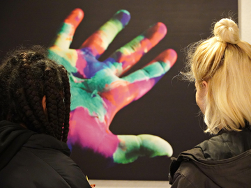 2 Frauen schauen auf ein Foto mit einer bunten Hand