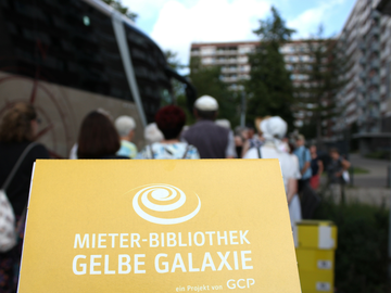 Menschen stehen vor einem Bus. Auf einem Schild steht "Mieter-Bibliothek Gelbe Galaxie". 