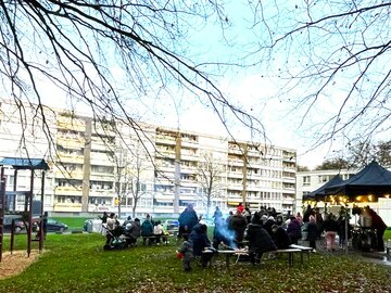 Kinder und Erwachsene sitzen gemeinschaftlich im Freien, bei Lagerfeuer und anderen Aktivitäten zusammen. 