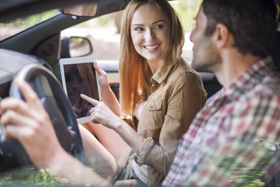 Eine Mann und eine Frau sitzen im Auto. Die Frau zeigt auf ein Tablet.